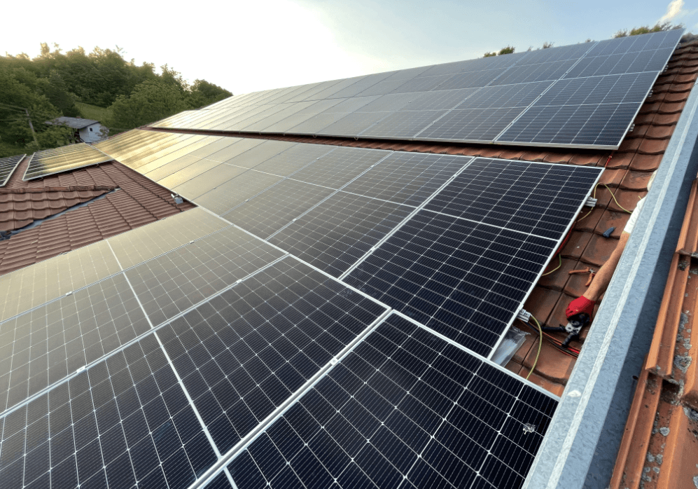 Solar panels being installed on a red tile roof with a worker connecting the wiring.